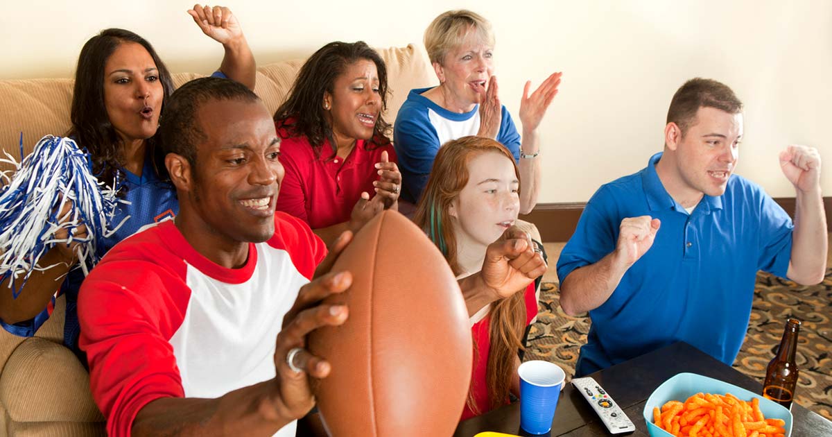 group of racially diverse football fans watching TV and cheering, they have snacks and are holding a football