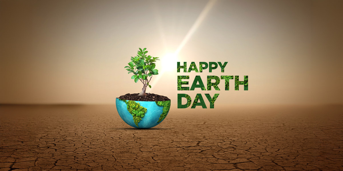 A small tree growing from a globe-shaped pot with "happy earth day" text, set against a sunlit, barren landscape.