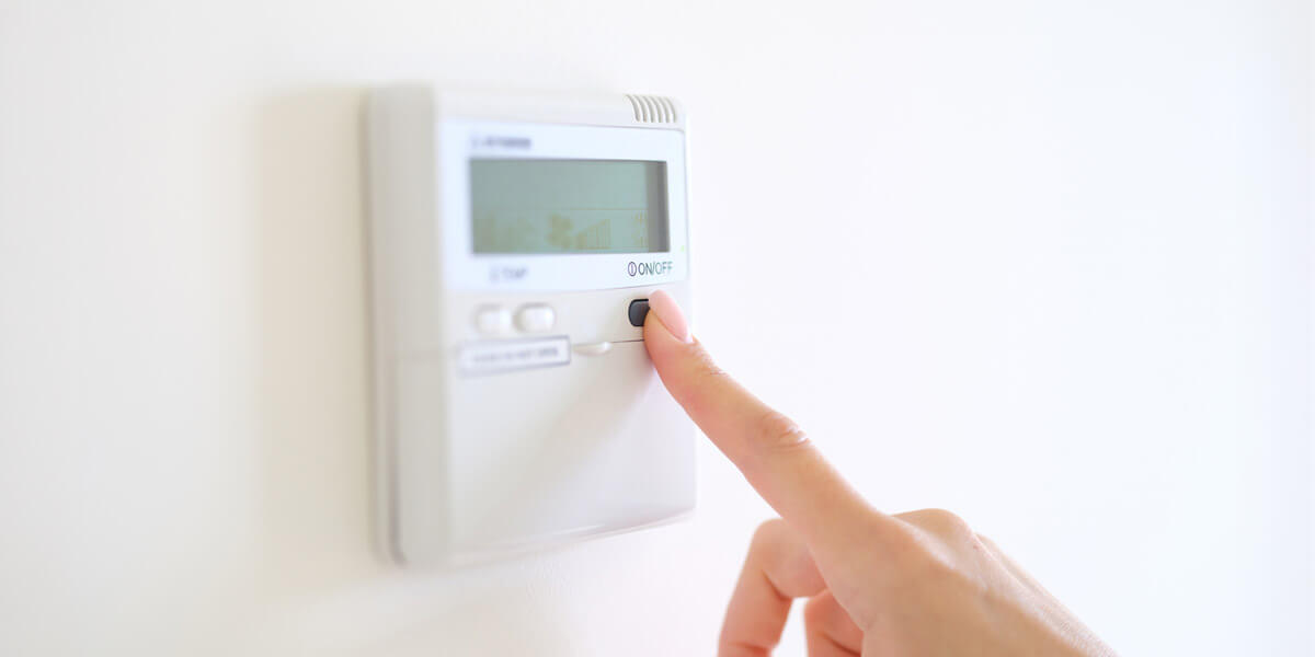 A person adjusting a wall thermostat to control the temperature.