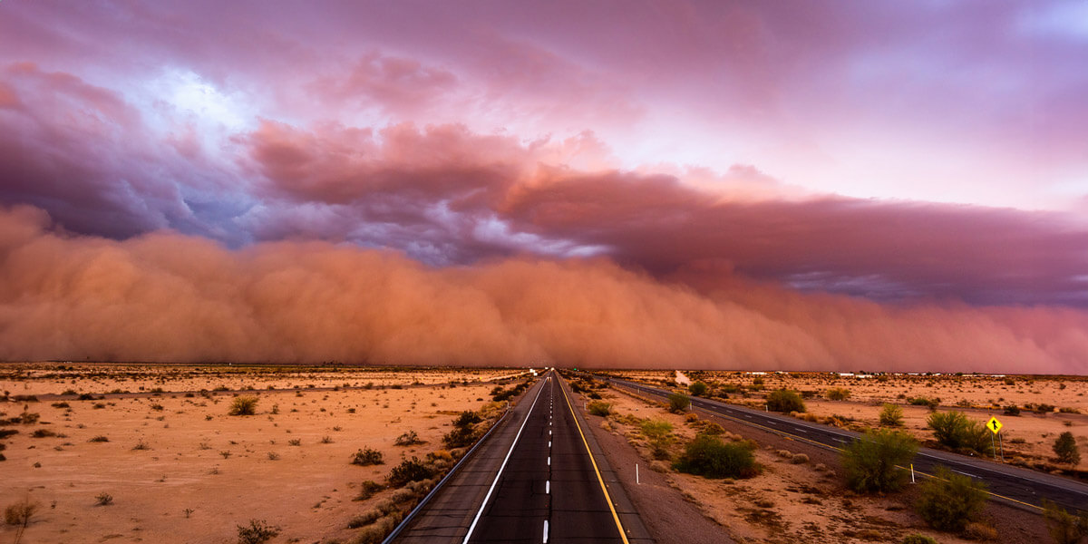 A sand storm looms over a desert road, creating a hazy and ominous atmosphere.
