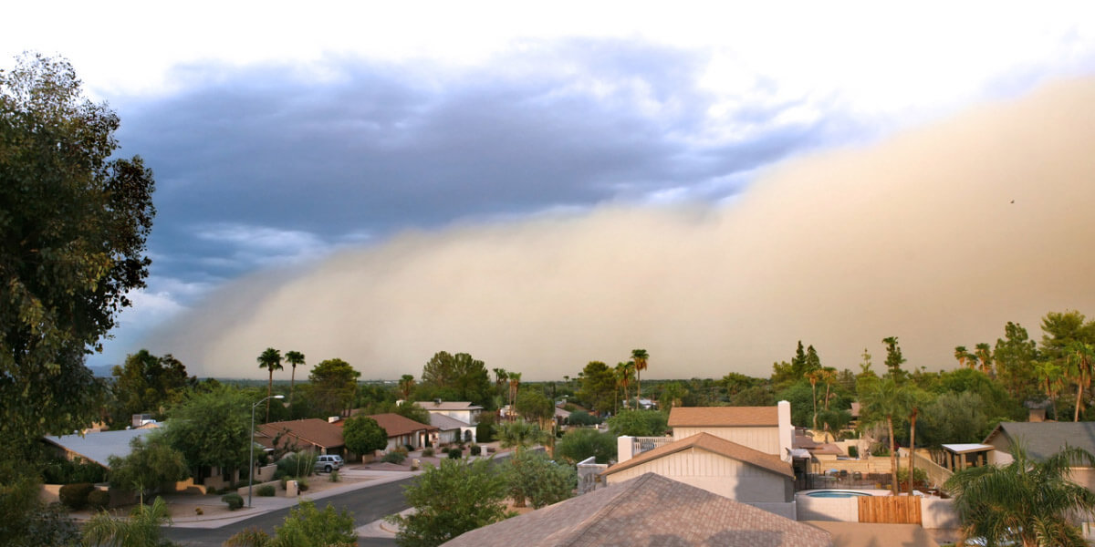 A dust storm engulfs a residential area, obscuring homes and creating a hazy atmosphere in the neighborhood.