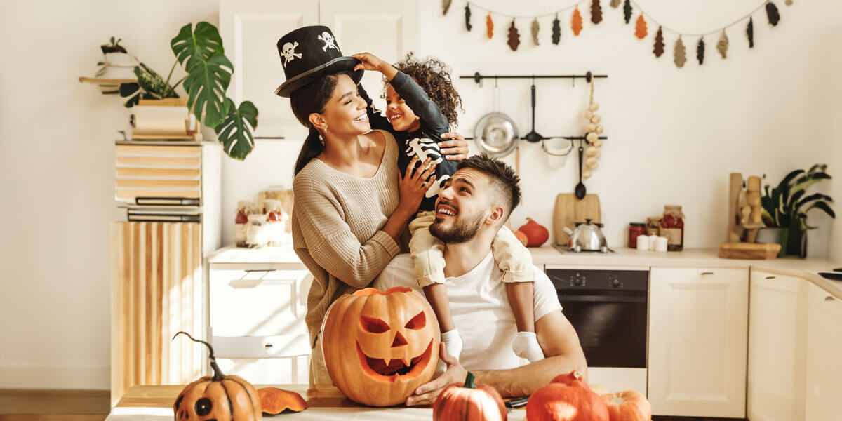 A family gathers in a kitchen adorned with festive Halloween decorations, creating a warm and cheerful atmosphere.